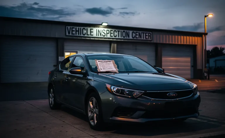 Une voiture est stationnée devant un centre de contrôle technique fermé au crépuscule, avec une vignette expirée et un reçu de rendez-vous sur le pare-brise.