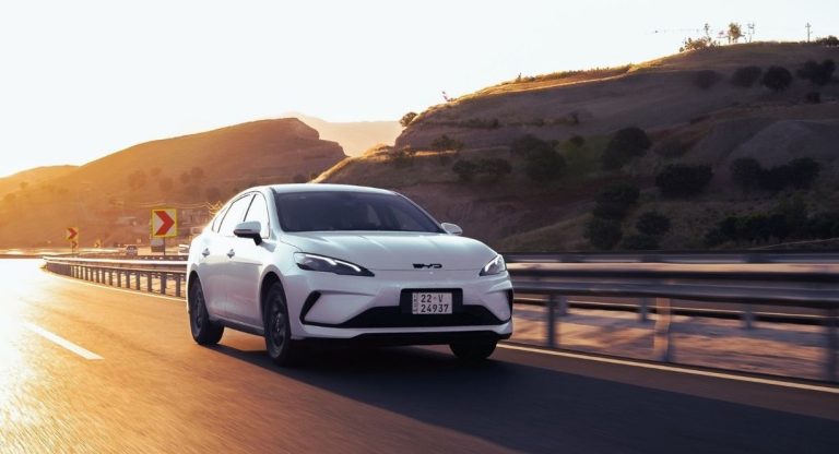 Voiture electrique blanche roulant sur une route de montagne au coucher du soleil